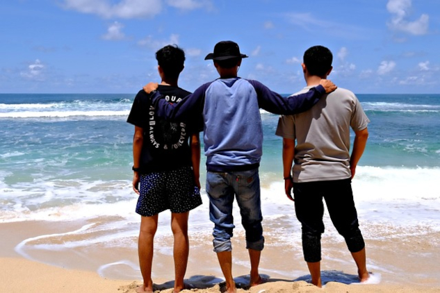 Three men standing together on the beach facing the ocean. Image by hartono subagio from Pixabay.&nbsp;